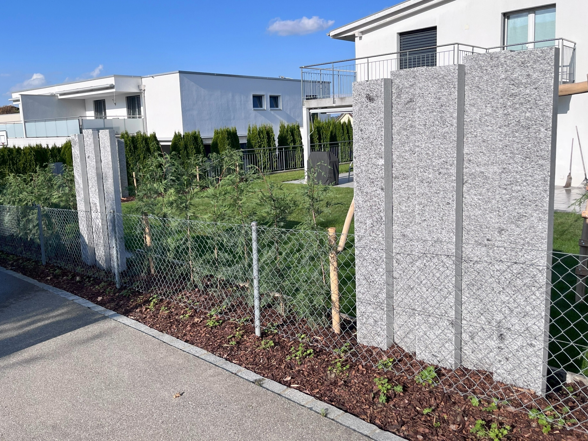 Leyland-Zypressen Hecke mit Gneisstelen entlang der Straße